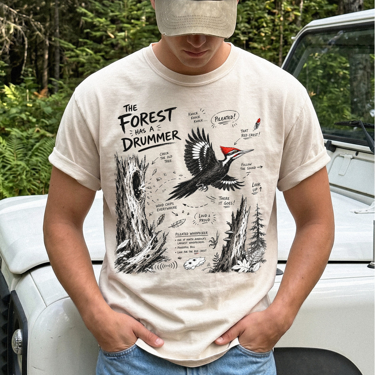 The Forest Has a Drummer Comfort Colors Shirt – Pileated Woodpecker design of a Pileated Woodpecker illustrated in flight with its vivid red crest, surrounded by old tree trunks, wood chips, and forest details, printed on an Ivory T-shirt.