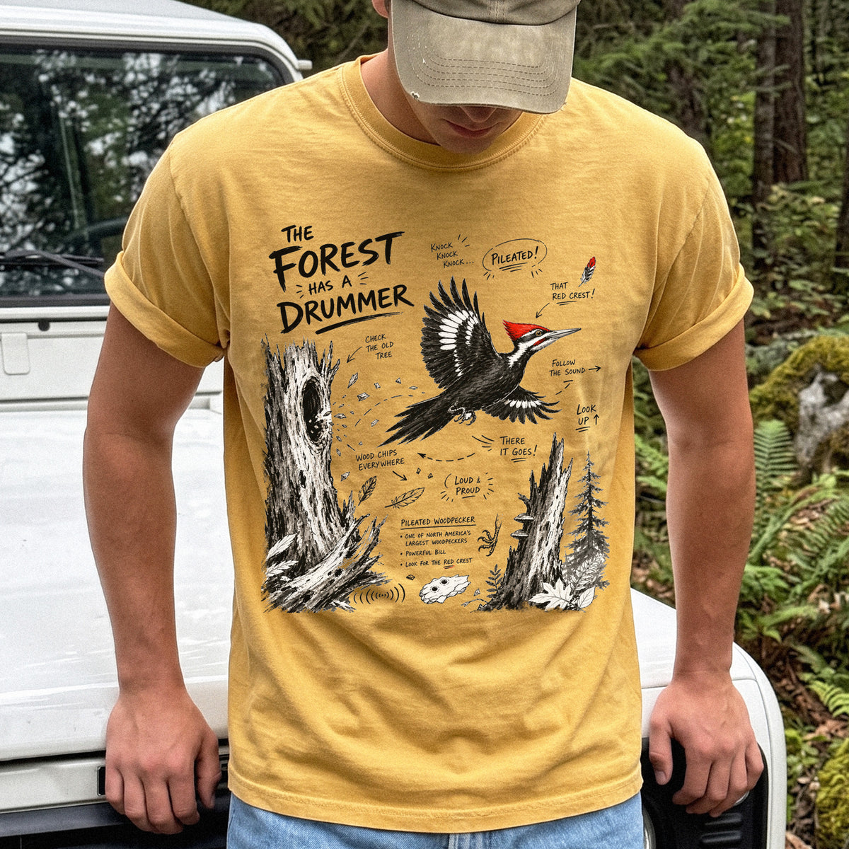 The Forest Has a Drummer Comfort Colors Shirt – Pileated Woodpecker design of a Pileated Woodpecker illustrated in flight with its vivid red crest, surrounded by old tree trunks, wood chips, and forest details, printed on a Mustard T-shirt.
