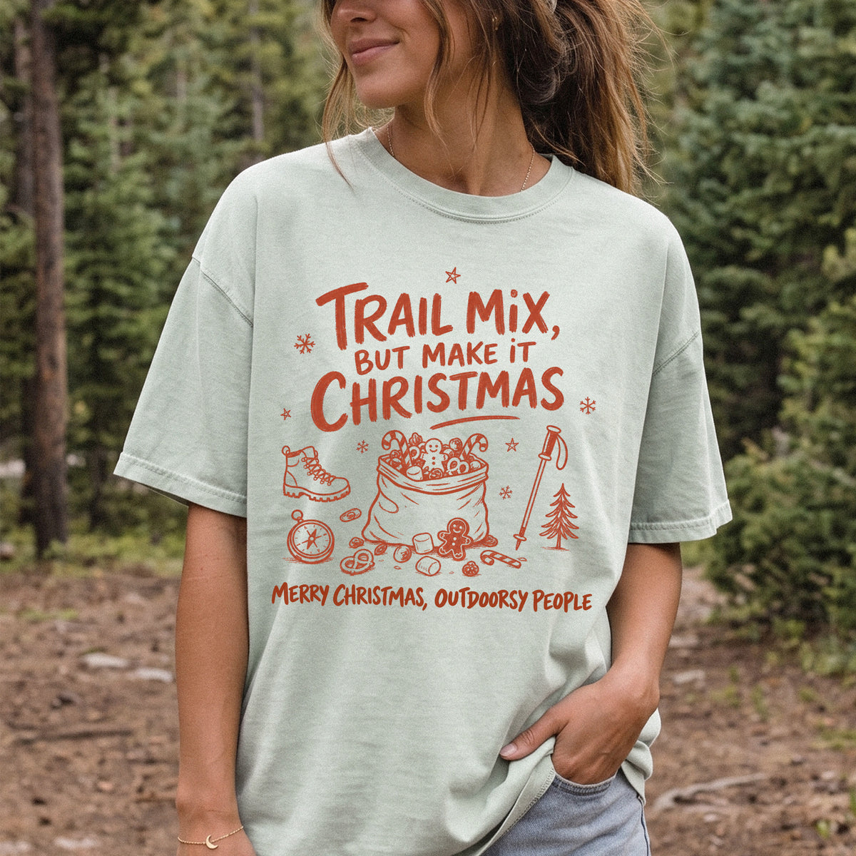 Woman wearing a Bay T-shirt printed with festive trail snacks, candy canes, a gingerbread cookie, a hiking boot, compass, and trekking pole, doodle style
