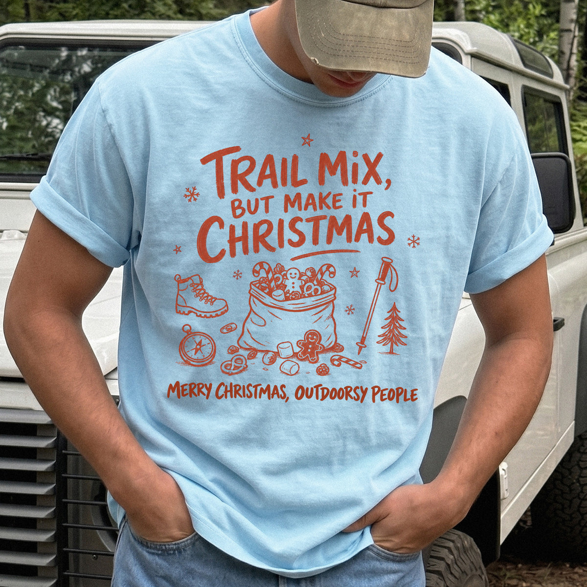Man wearing a Chambray T-shirt printed with festive trail snacks, candy canes, a gingerbread cookie, a hiking boot, compass, and trekking pole, doodle style