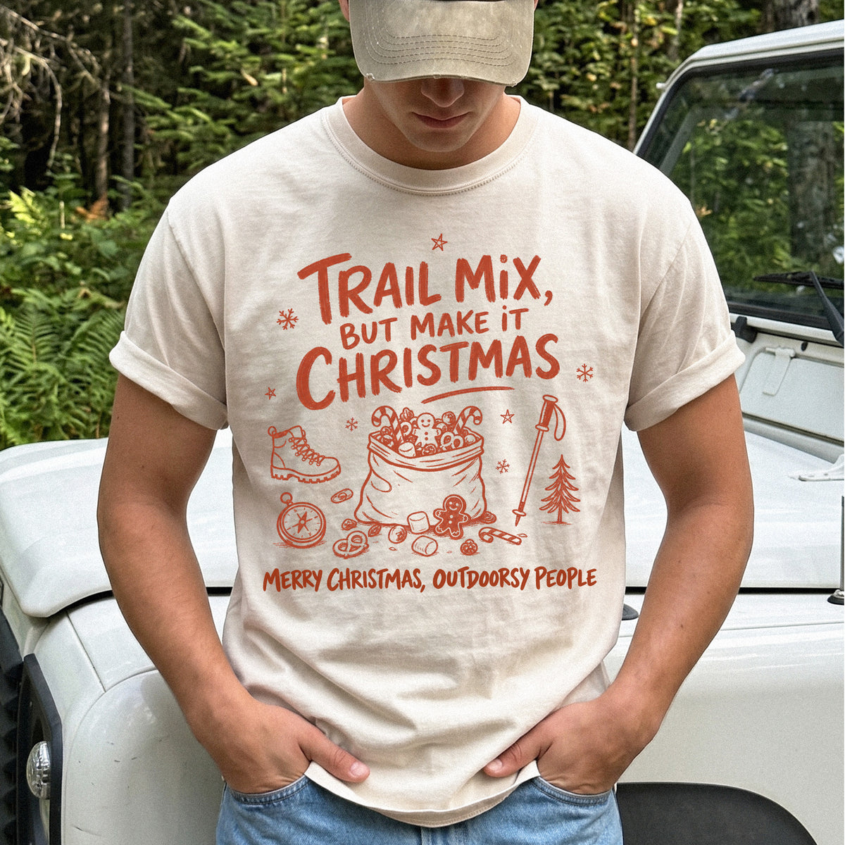 Man wearing an Ivory T-shirt printed with festive trail snacks, candy canes, a gingerbread cookie, a hiking boot, compass, and trekking pole, doodle style