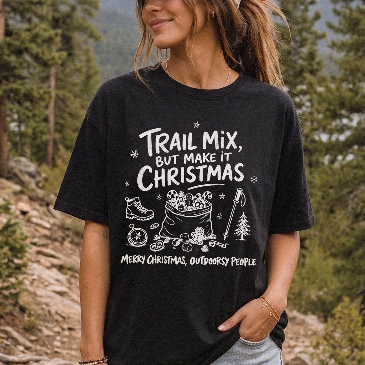 Woman wearing a Black T-shirt printed with festive trail snacks, candy canes, a gingerbread cookie, a hiking boot, compass, and trekking pole, doodle style