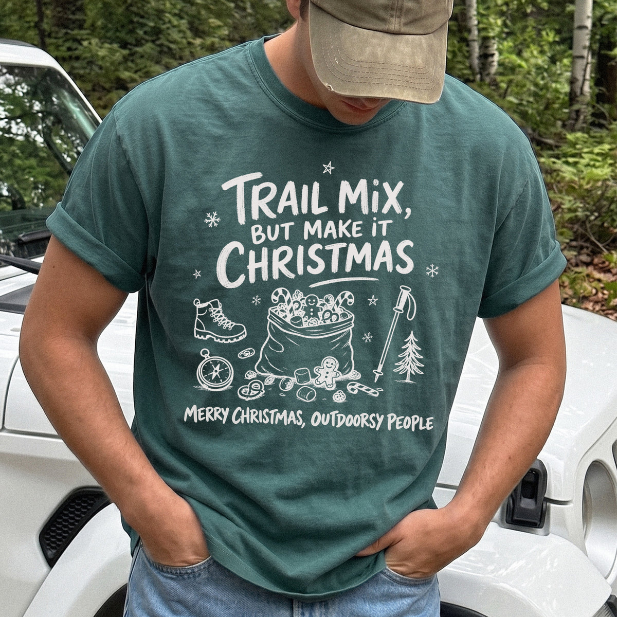 Man wearing a Blue Spruce T-shirt printed with festive trail snacks, candy canes, a gingerbread cookie, a hiking boot, compass, and trekking pole, doodle style