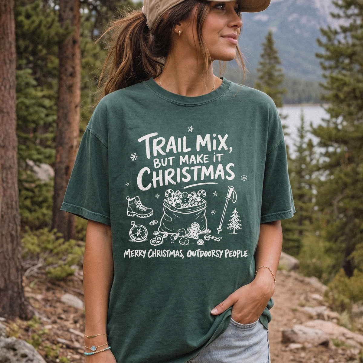 Woman wearing a Blue Spruce T-shirt printed with festive trail snacks, candy canes, a gingerbread cookie, a hiking boot, compass, and trekking pole, doodle style