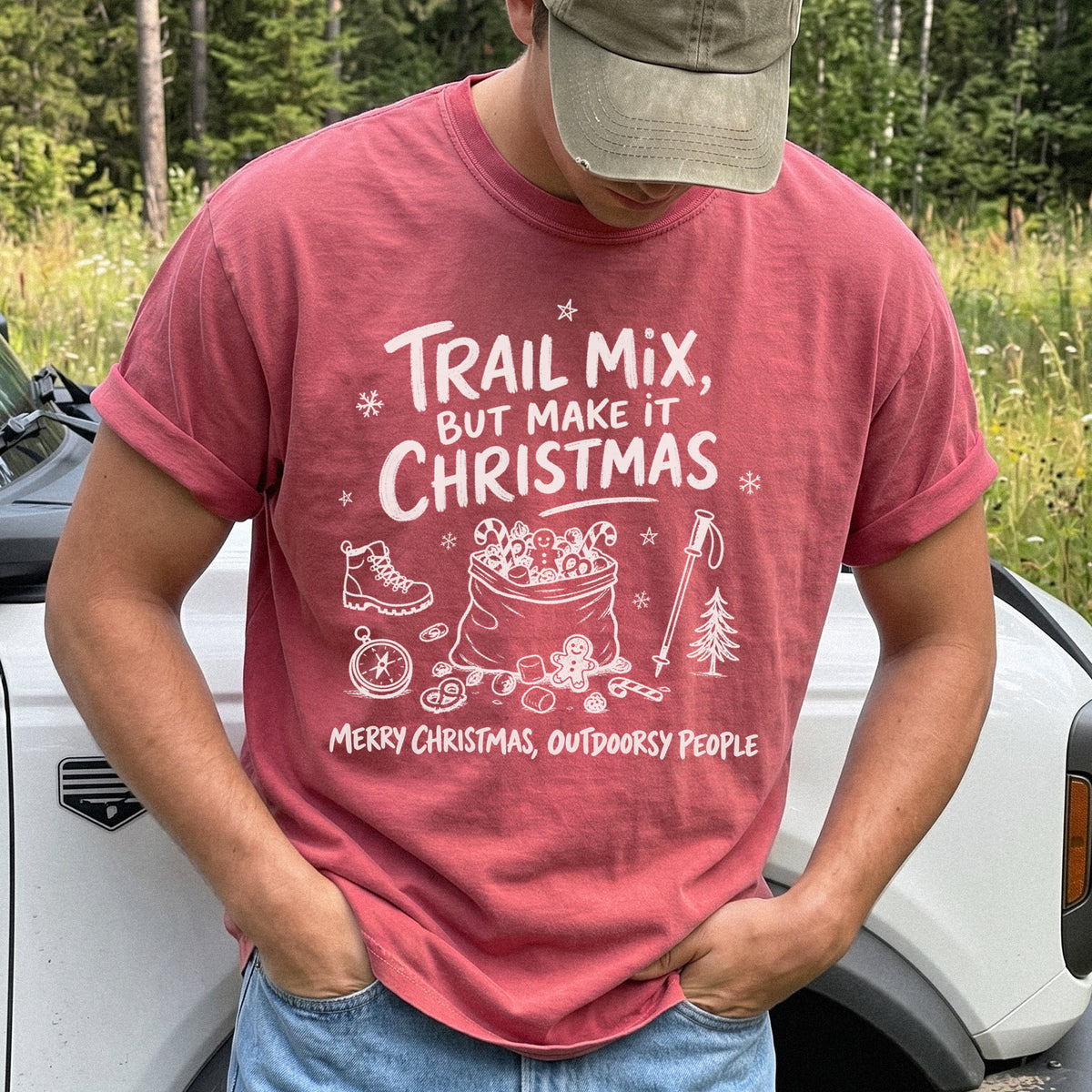 Man wearing a Crimson T-shirt printed with festive trail snacks, candy canes, a gingerbread cookie, a hiking boot, compass, and trekking pole, doodle style