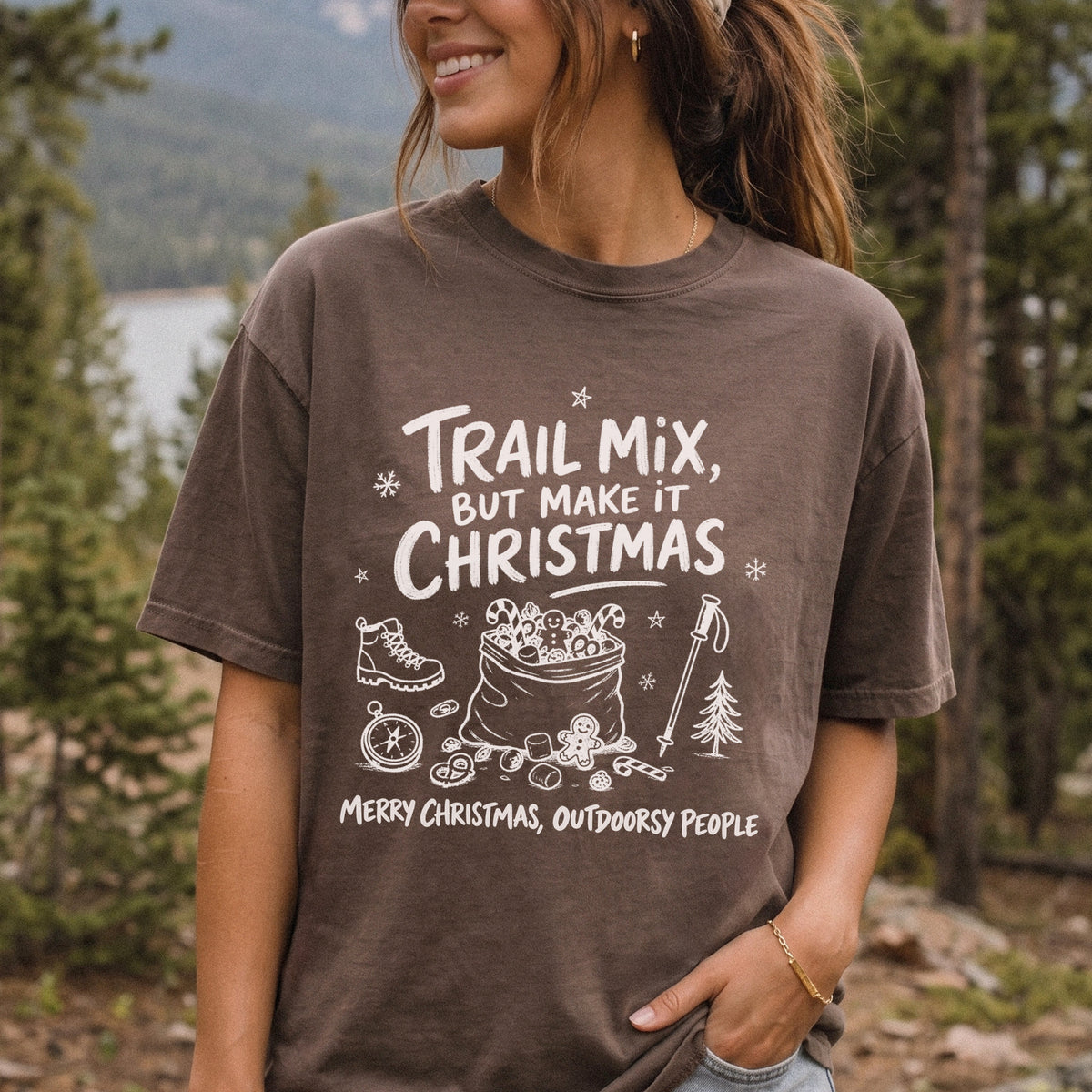 Woman wearing an Espresso T-shirt printed with festive trail snacks, candy canes, a gingerbread cookie, a hiking boot, compass, and trekking pole, doodle style