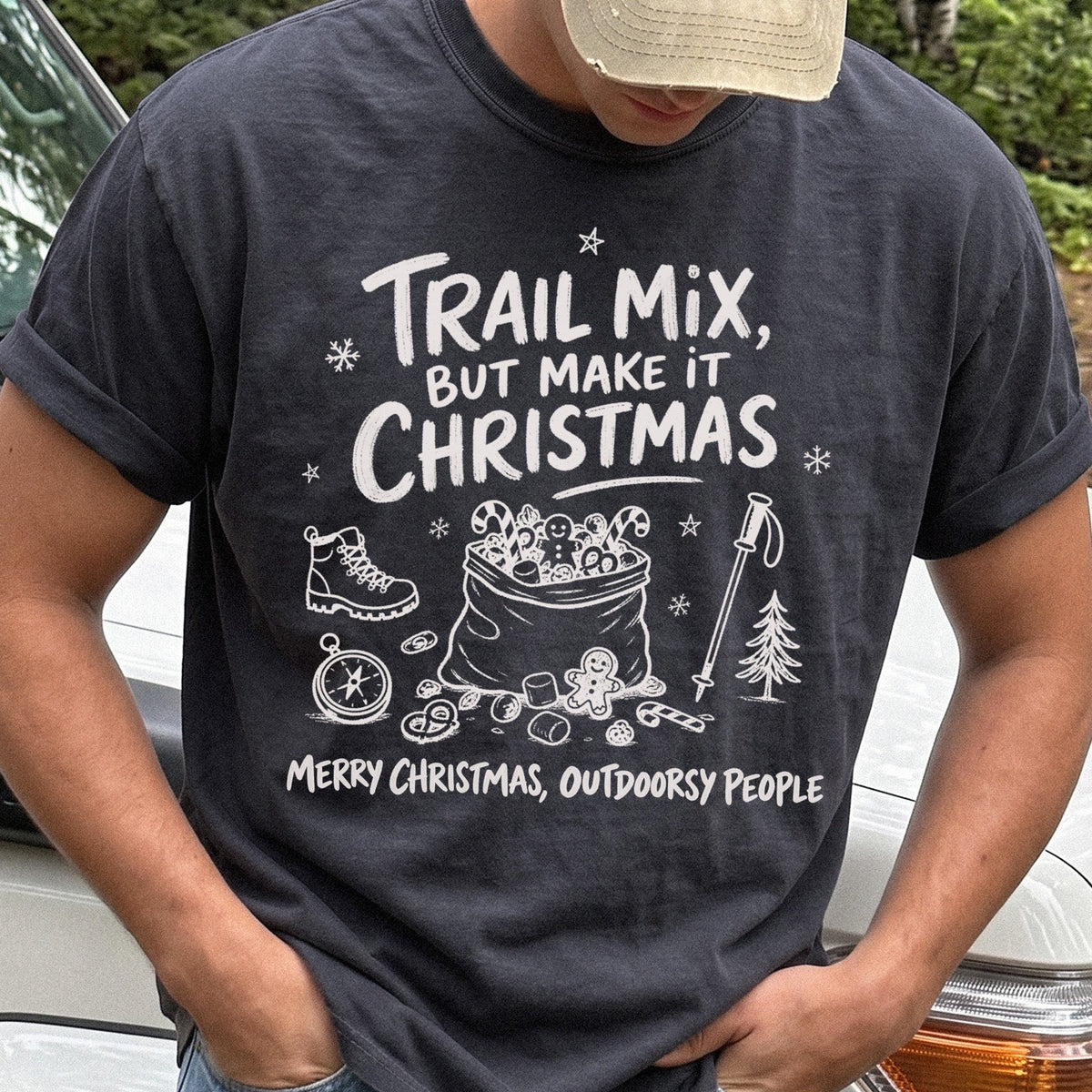 Man wearing a Graphite T-shirt printed with festive trail snacks, candy canes, a gingerbread cookie, a hiking boot, compass, and trekking pole, doodle style