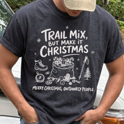 Man wearing a Graphite T-shirt printed with festive trail snacks, candy canes, a gingerbread cookie, a hiking boot, compass, and trekking pole, doodle style