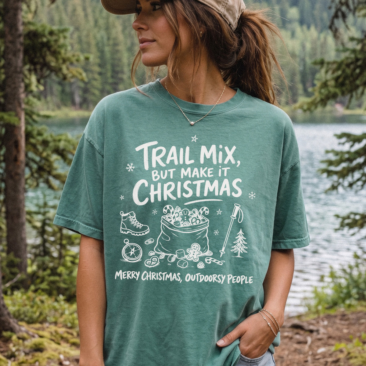 Woman wearing a Light Green T-shirt printed with festive trail snacks, candy canes, a gingerbread cookie, a hiking boot, compass, and trekking pole, doodle style