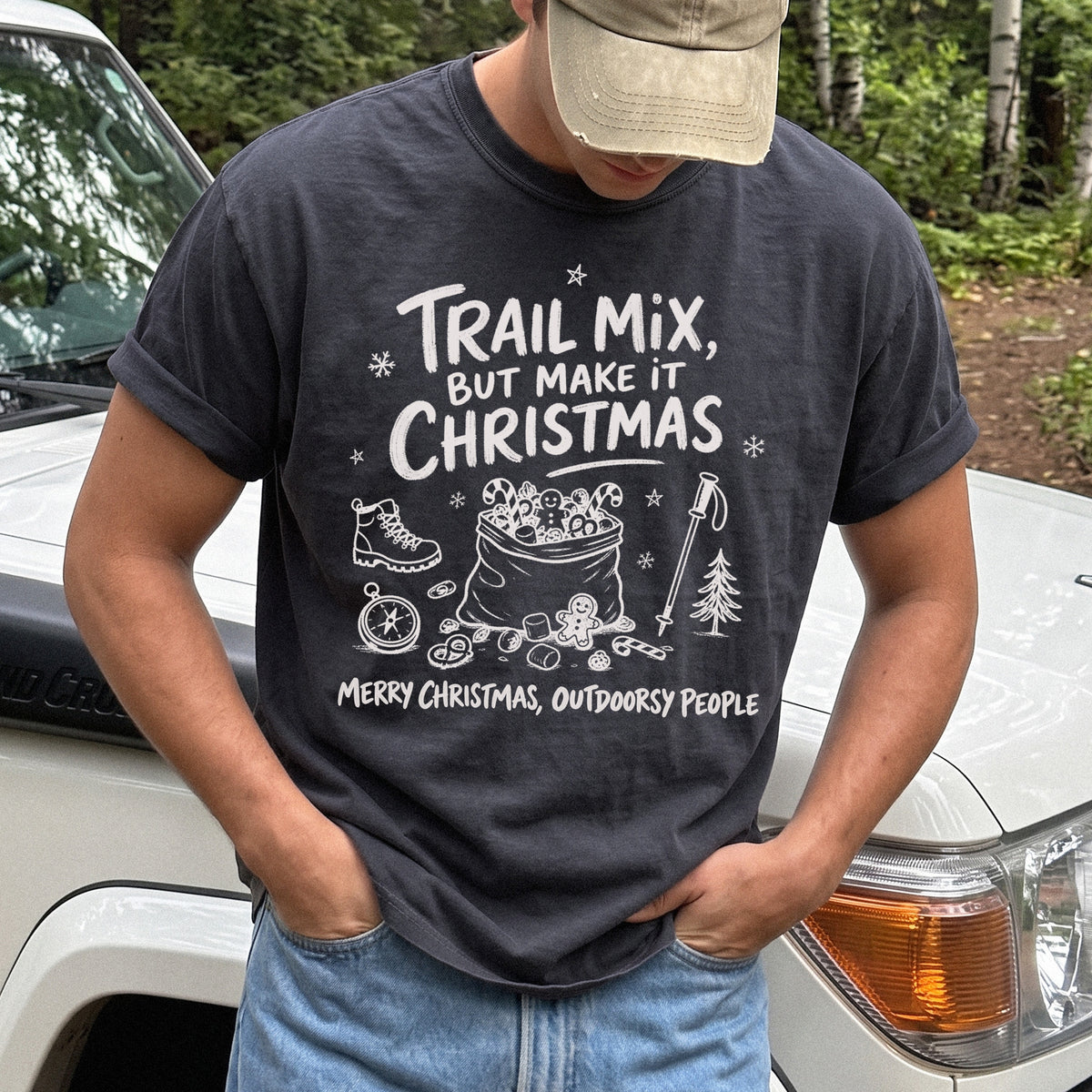 Man wearing a Graphite T-shirt printed with festive trail snacks, candy canes, a gingerbread cookie, a hiking boot, compass, and trekking pole, doodle style